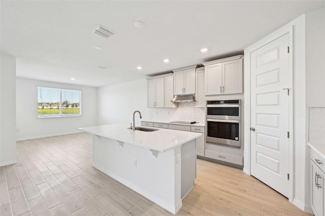 kitchen featuring wood finish floors, a sink, under cabinet range hood, double oven, and black electric cooktop