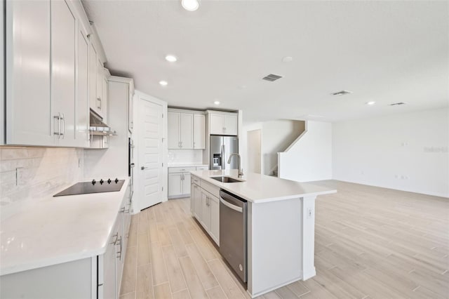 kitchen with wood finish floors, a sink, under cabinet range hood, backsplash, and appliances with stainless steel finishes