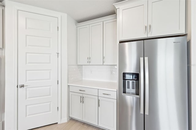 kitchen with backsplash, light wood-style flooring, stainless steel refrigerator with ice dispenser, and light countertops