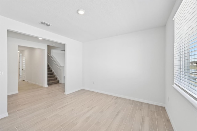 empty room featuring light wood finished floors, visible vents, stairs, and baseboards