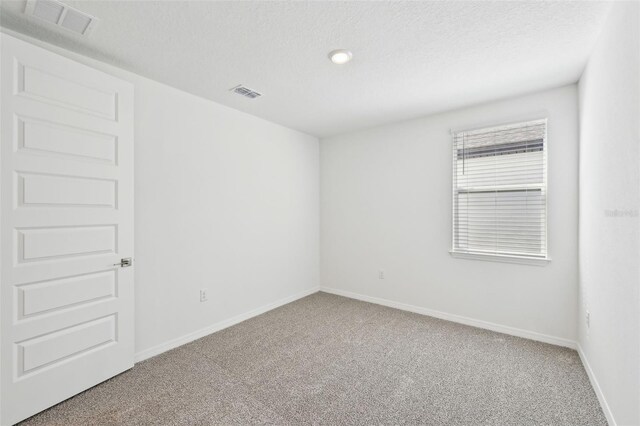 empty room featuring visible vents, carpet floors, a textured ceiling, and baseboards