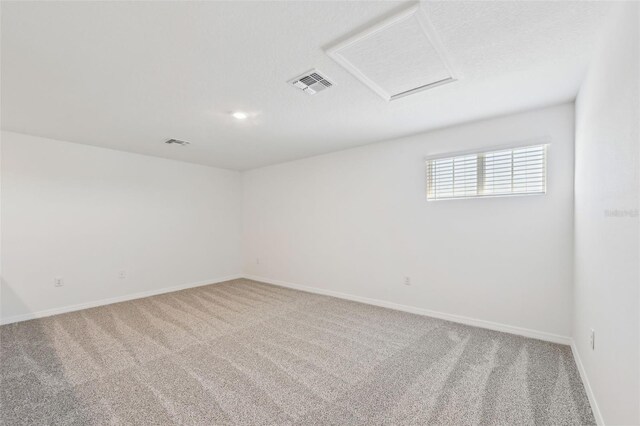 carpeted empty room featuring attic access, baseboards, and visible vents