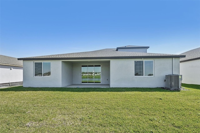 rear view of property featuring a lawn, cooling unit, roof with shingles, and stucco siding