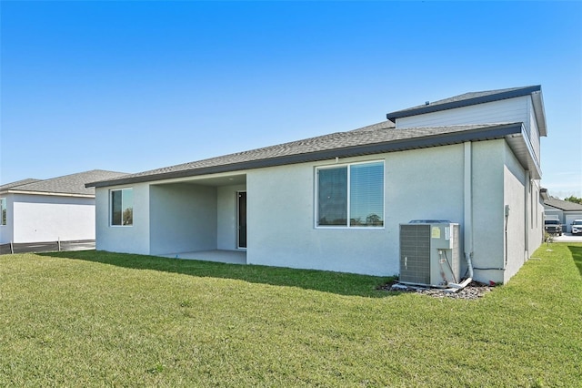 back of property featuring central air condition unit, stucco siding, a shingled roof, and a yard