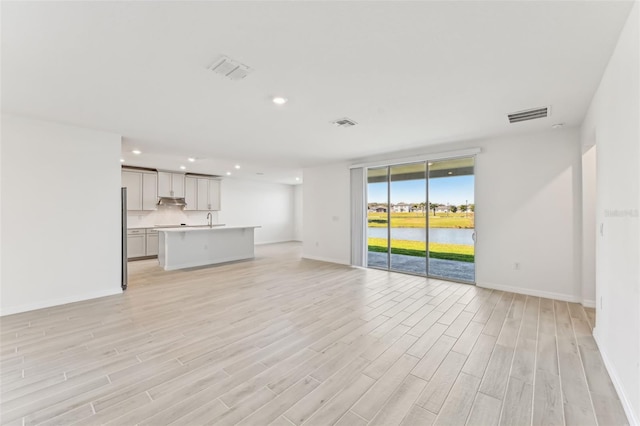 unfurnished living room with a water view, light hardwood / wood-style floors, and sink