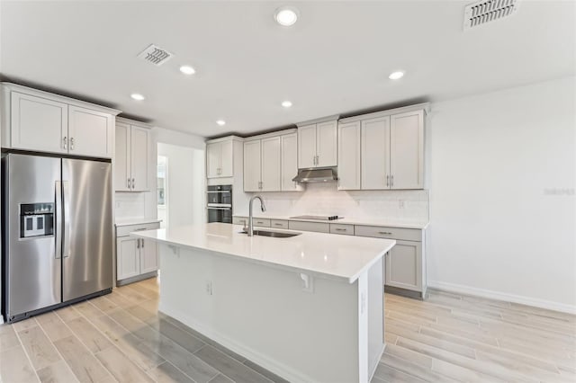 kitchen featuring light wood-type flooring, a kitchen island with sink, black appliances, and sink