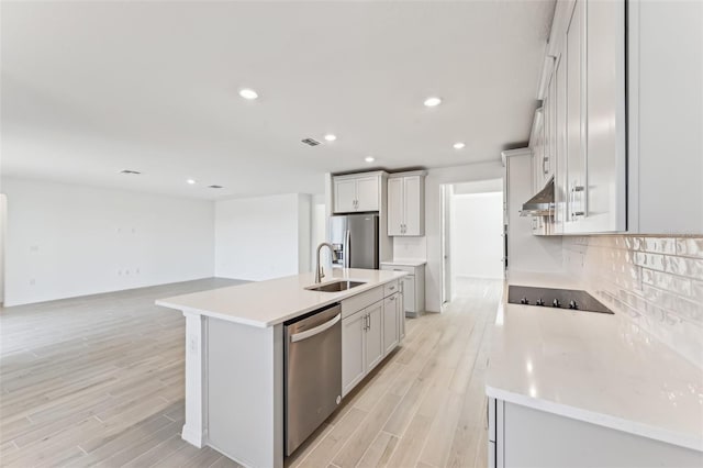 kitchen with a center island with sink, appliances with stainless steel finishes, decorative backsplash, sink, and light hardwood / wood-style flooring