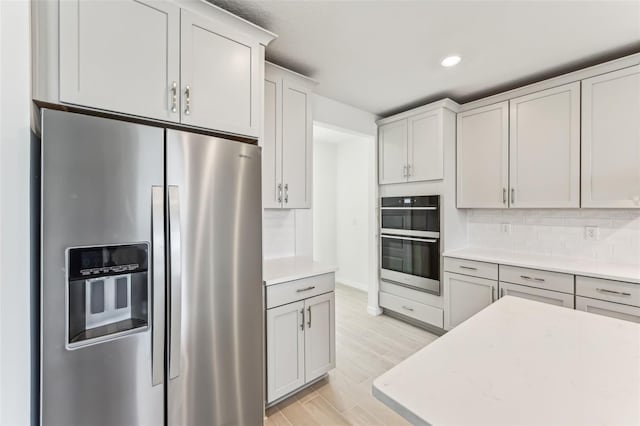 kitchen featuring stainless steel appliances, light wood-type flooring, backsplash, and white cabinetry