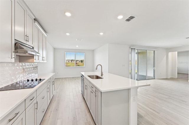 kitchen with sink, light hardwood / wood-style floors, stainless steel dishwasher, black electric cooktop, and a kitchen island with sink