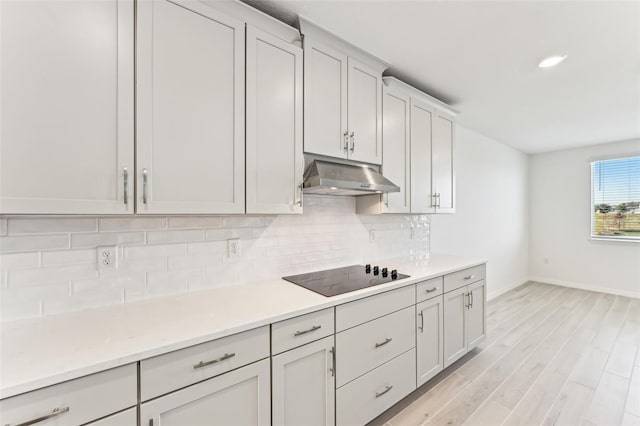 kitchen featuring backsplash, black electric stovetop, light hardwood / wood-style floors, and light stone countertops