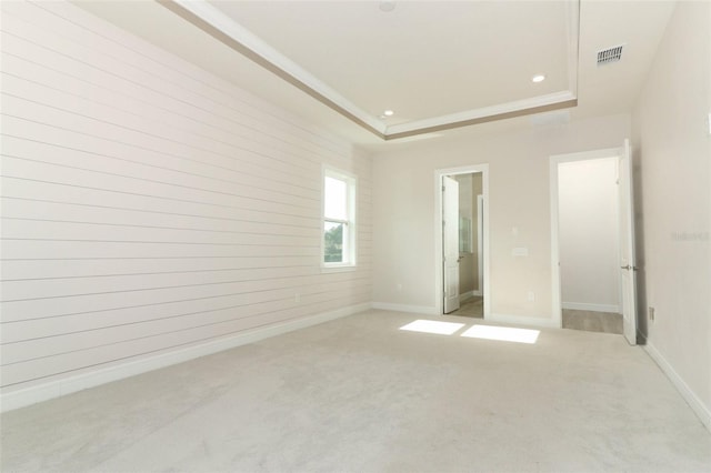 unfurnished bedroom featuring ensuite bathroom, a raised ceiling, and light colored carpet