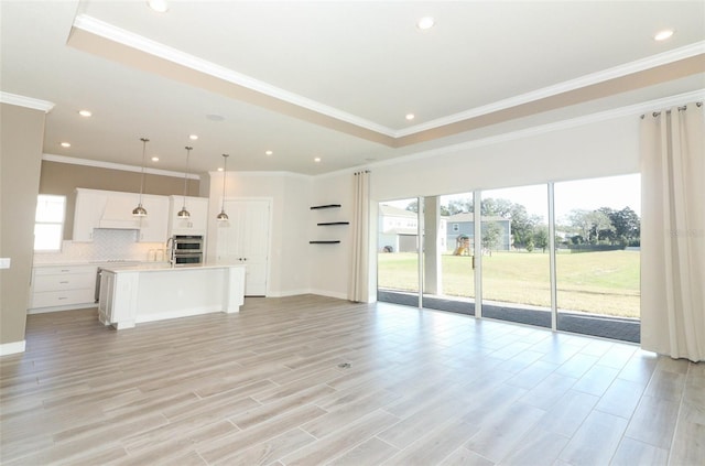 unfurnished living room with a raised ceiling, light wood-type flooring, and crown molding