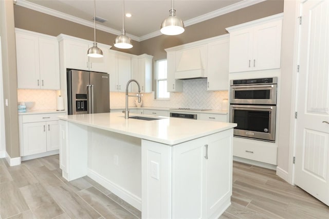 kitchen featuring stainless steel appliances, sink, decorative light fixtures, a center island with sink, and white cabinetry