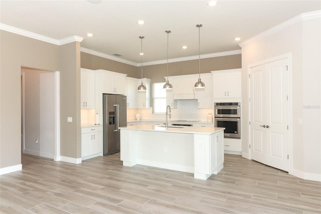 kitchen featuring appliances with stainless steel finishes, white cabinetry, a kitchen island with sink, and pendant lighting