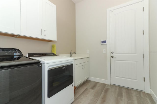 clothes washing area featuring washing machine and clothes dryer, cabinets, sink, and light hardwood / wood-style floors