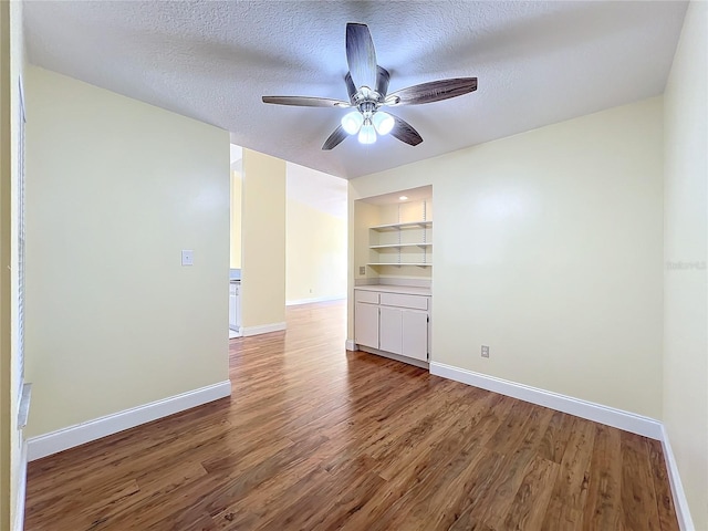 empty room featuring a textured ceiling, built in features, ceiling fan, and dark wood-type flooring