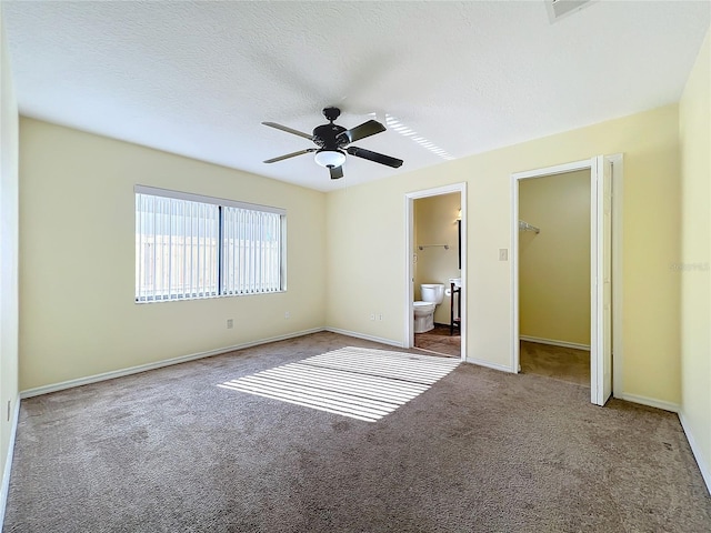 unfurnished bedroom featuring ensuite bath, a spacious closet, ceiling fan, carpet floors, and a closet