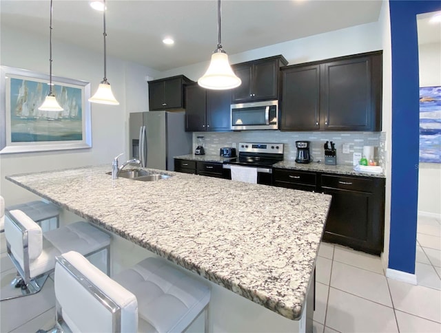 kitchen with appliances with stainless steel finishes, a center island with sink, and decorative light fixtures