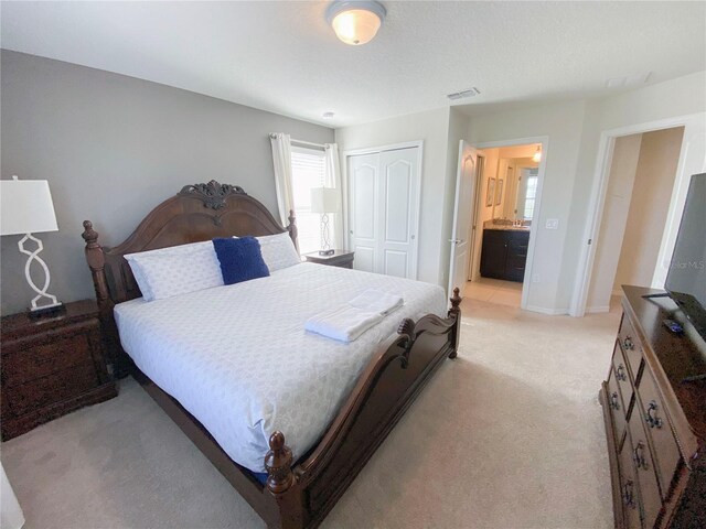 bedroom with ensuite bath, light carpet, and a closet