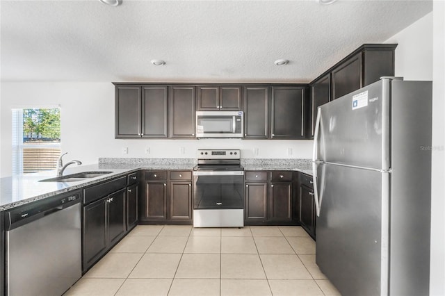 kitchen featuring appliances with stainless steel finishes, light tile patterned flooring, dark brown cabinets, light stone countertops, and sink