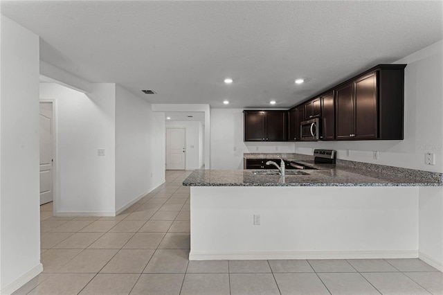 kitchen with dark stone countertops, kitchen peninsula, sink, appliances with stainless steel finishes, and dark brown cabinets