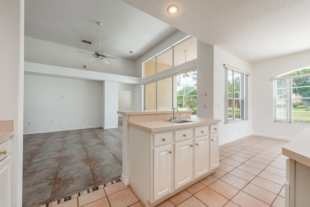 kitchen with sink, ceiling fan, a textured ceiling, light tile patterned flooring, and white cabinetry