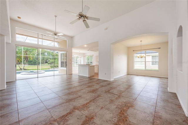 unfurnished room featuring ceiling fan with notable chandelier, a healthy amount of sunlight, light tile patterned flooring, and a high ceiling