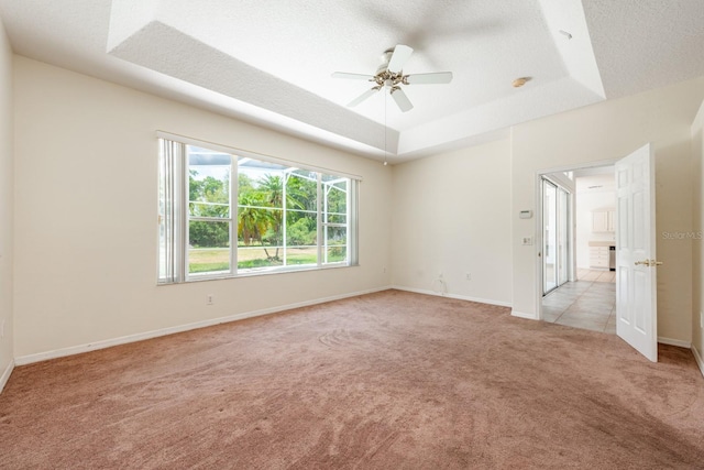 unfurnished room featuring a textured ceiling, ceiling fan, light carpet, and a tray ceiling