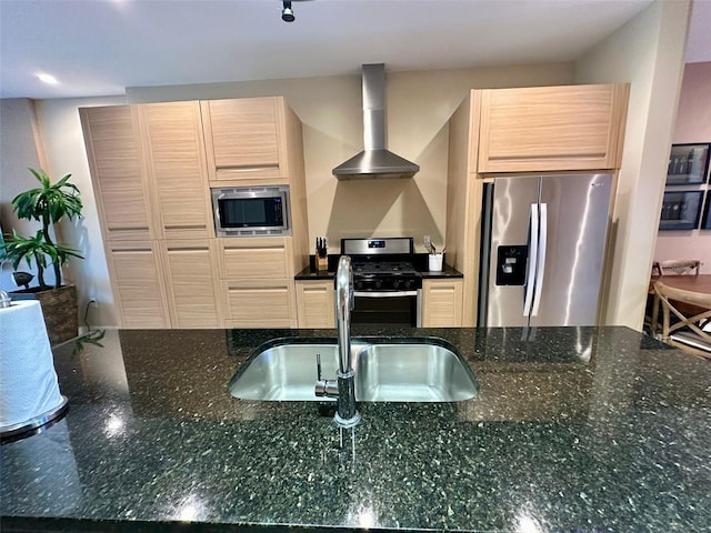 kitchen featuring sink, wall chimney exhaust hood, dark stone countertops, light brown cabinetry, and stainless steel appliances