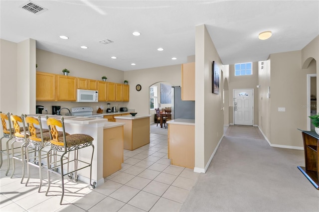 kitchen featuring white appliances, light tile patterned floors, light brown cabinetry, kitchen peninsula, and a breakfast bar area