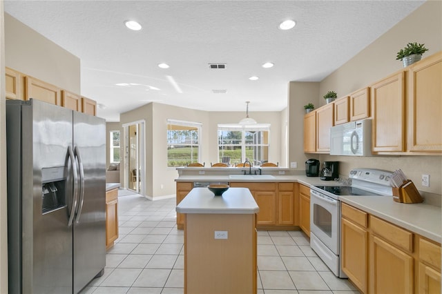 kitchen featuring white appliances, sink, light brown cabinetry, decorative light fixtures, and a kitchen island