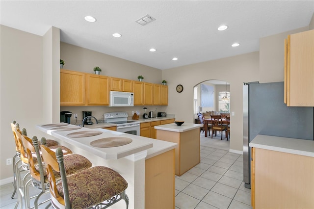 kitchen with light tile patterned flooring, white appliances, a kitchen island, a kitchen bar, and kitchen peninsula