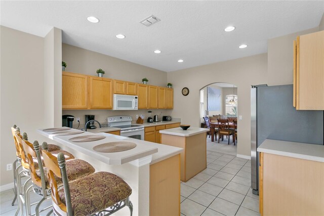 128 Higher Combe Dr, Davenport, FL 33897 - kitchen with white appliances, a kitchen island, arched walkways, light countertops, and light brown cabinets