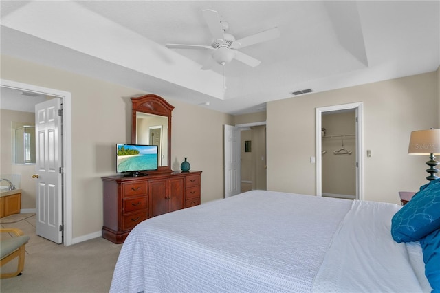 carpeted bedroom with a raised ceiling, ceiling fan, a spacious closet, connected bathroom, and a closet