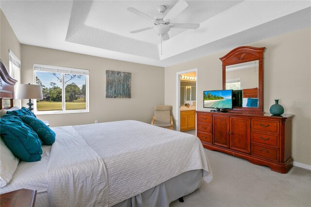 carpeted bedroom featuring ensuite bathroom, a raised ceiling, and ceiling fan