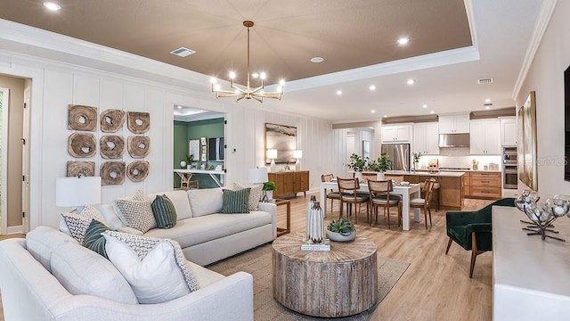 living room featuring a chandelier, light hardwood / wood-style floors, a raised ceiling, and ornamental molding