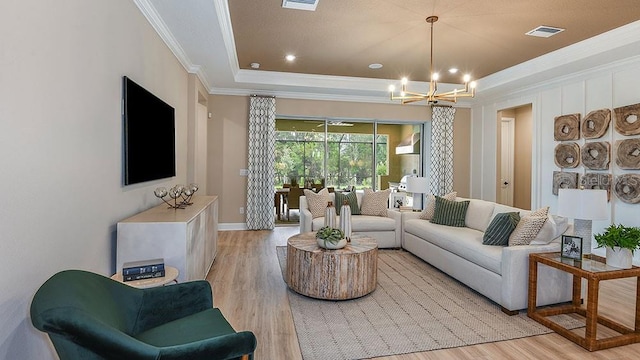 living room with a tray ceiling, crown molding, a notable chandelier, and light hardwood / wood-style flooring