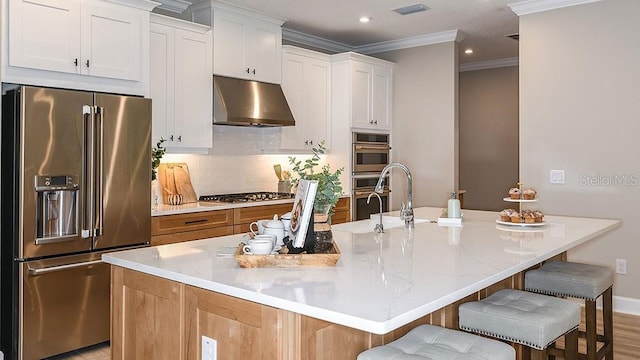 kitchen featuring stainless steel appliances, extractor fan, a center island with sink, white cabinetry, and a breakfast bar area