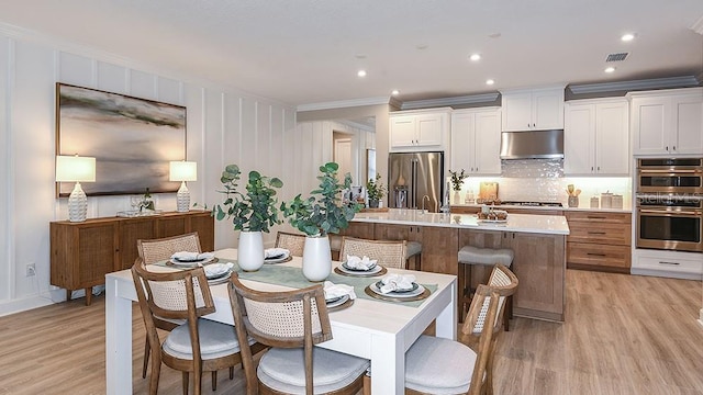 dining area featuring light hardwood / wood-style flooring, crown molding, and sink