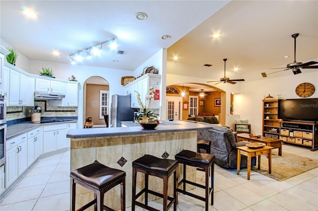 kitchen featuring white cabinetry, black cooktop, backsplash, and stainless steel refrigerator