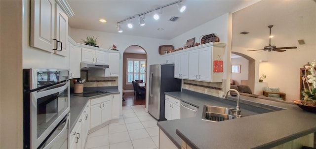 kitchen with stainless steel appliances, dark countertops, arched walkways, and under cabinet range hood