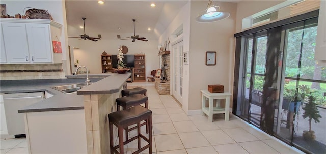 kitchen with a sink, dishwasher, a peninsula, light tile patterned flooring, and decorative backsplash