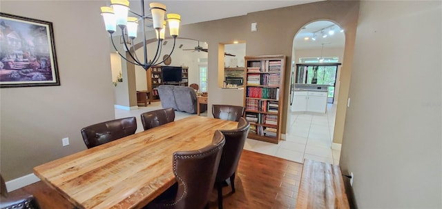 dining room featuring a chandelier, ceiling fan, arched walkways, tile patterned floors, and baseboards