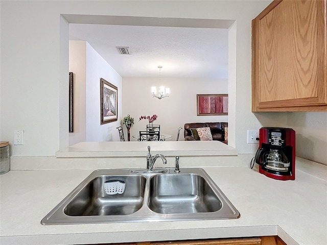 kitchen featuring sink, hanging light fixtures, a textured ceiling, and a notable chandelier