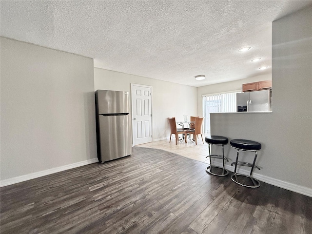 kitchen with stainless steel refrigerator with ice dispenser, a breakfast bar area, wood-type flooring, a textured ceiling, and stainless steel refrigerator