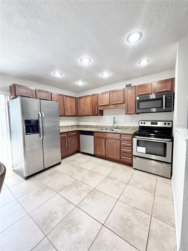 kitchen featuring sink, light tile patterned floors, stainless steel appliances, light stone counters, and a textured ceiling