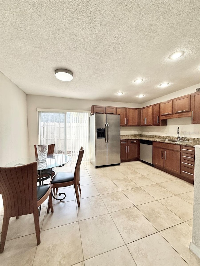 kitchen featuring appliances with stainless steel finishes, sink, light tile patterned floors, and a textured ceiling