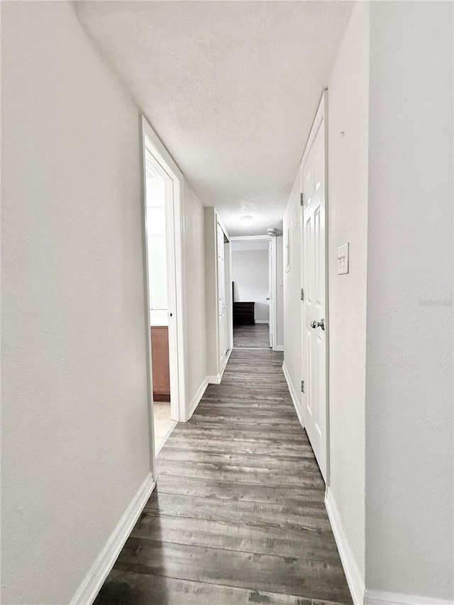 corridor with dark hardwood / wood-style floors and a textured ceiling