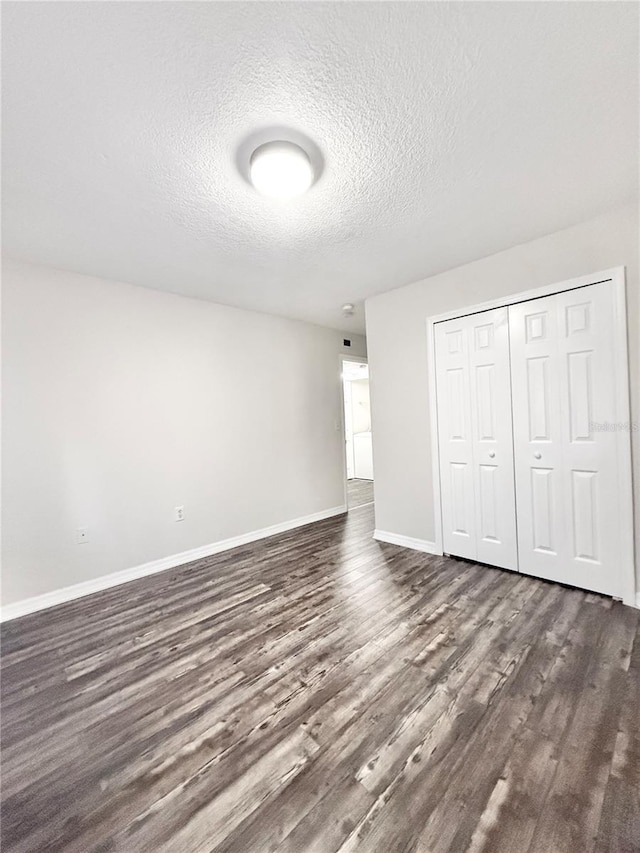 unfurnished bedroom with a textured ceiling, dark hardwood / wood-style flooring, and a closet