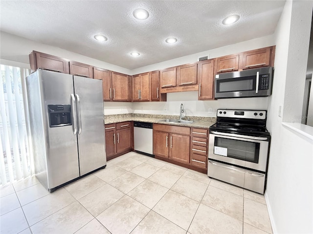 kitchen featuring appliances with stainless steel finishes, sink, light tile patterned floors, light stone countertops, and a textured ceiling